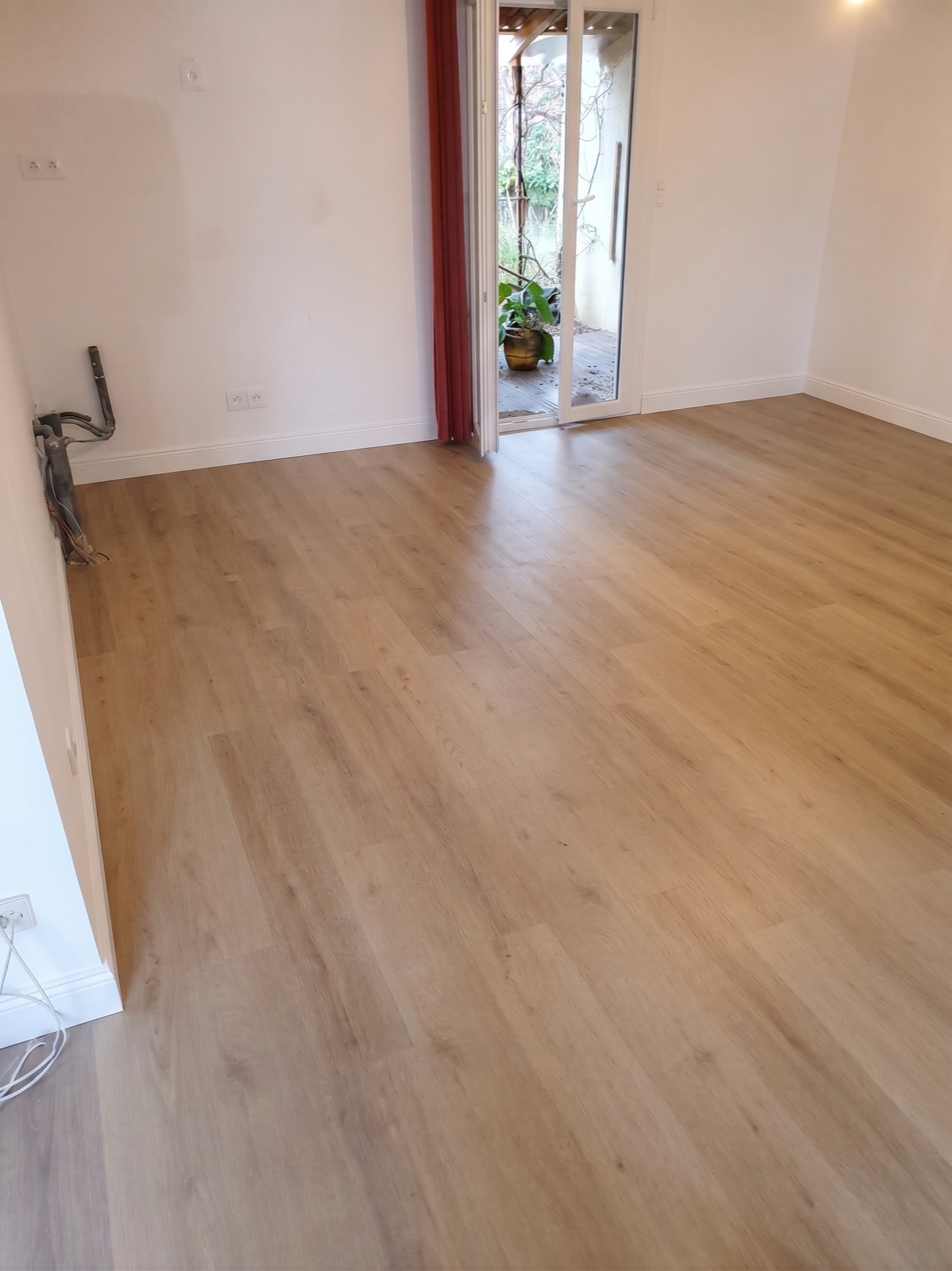 Pièce rénovée avec un parquet PVC aspect chêne clair, murs blancs et porte-fenêtre ouverte sur le jardin